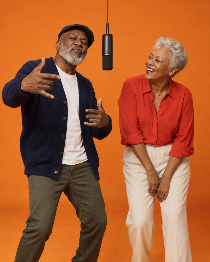 Older couple laughing and rapping beside a hanging microphone in an orange studio
